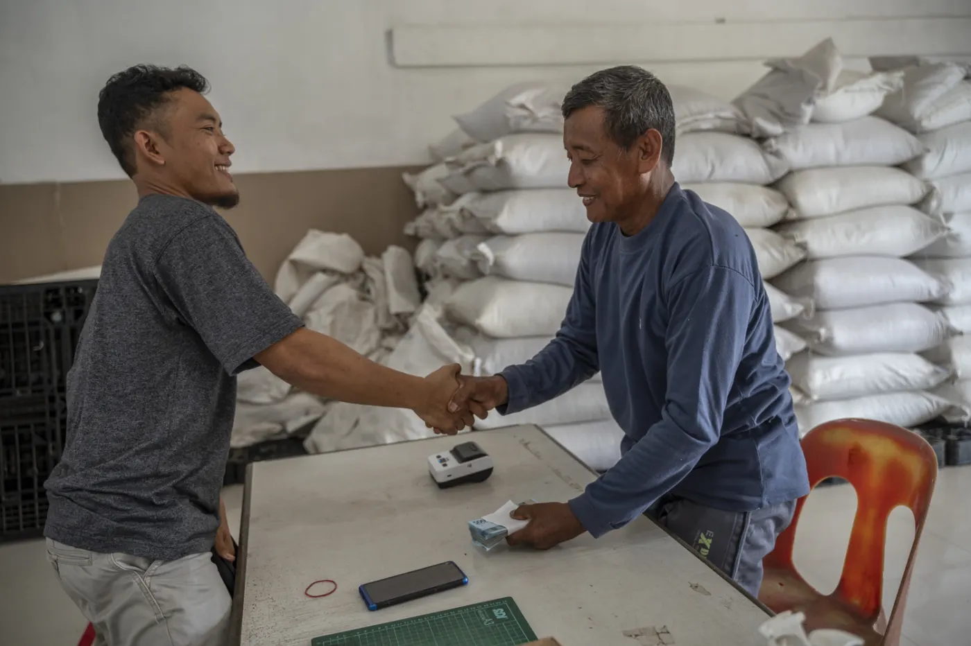 A farmer and a buyer shaking hands over a weighed, graded and recorded pepper delivery